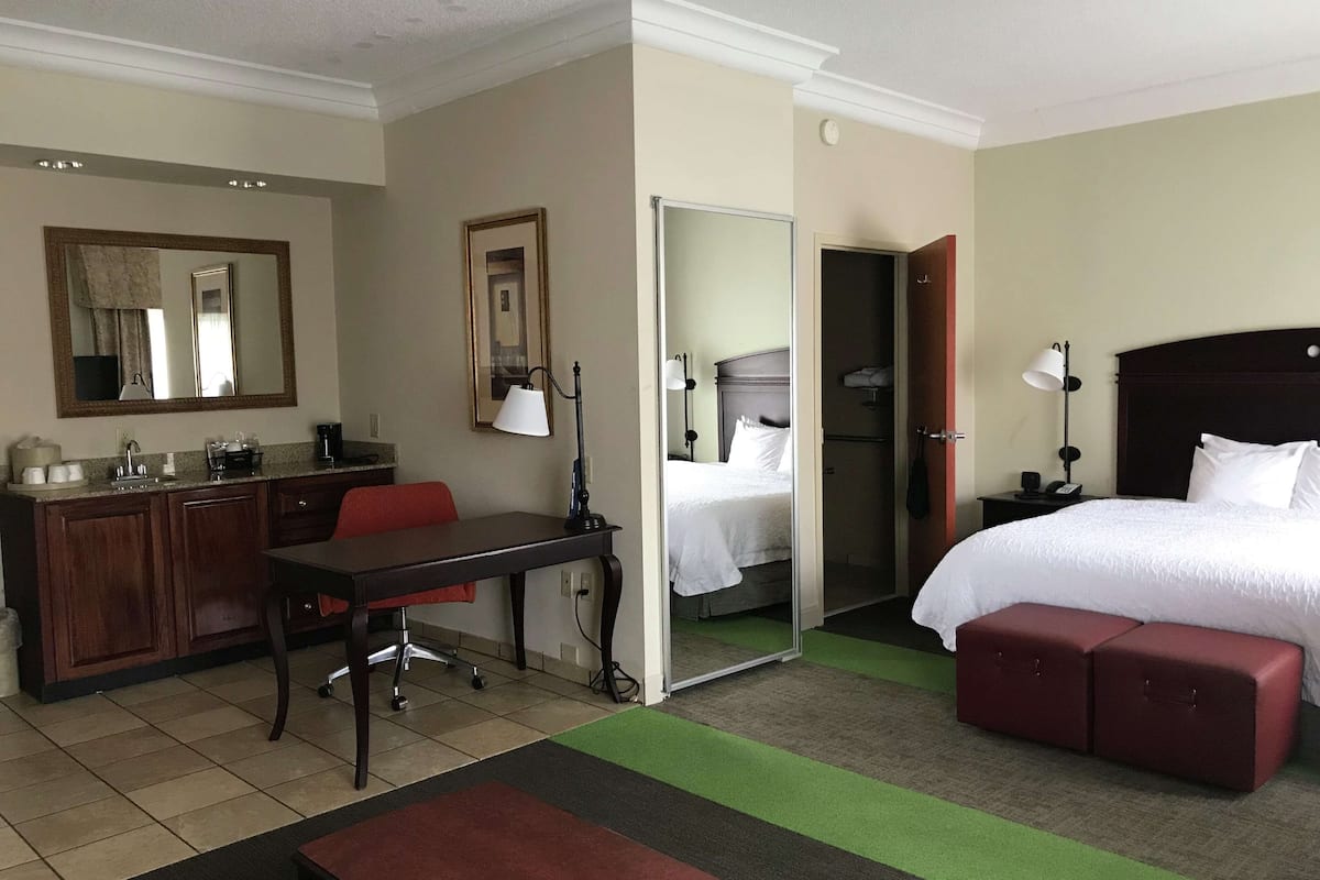 A hotel room with a bed, a desk, a chair, a mirror, a wardrobe, and a bathroom.