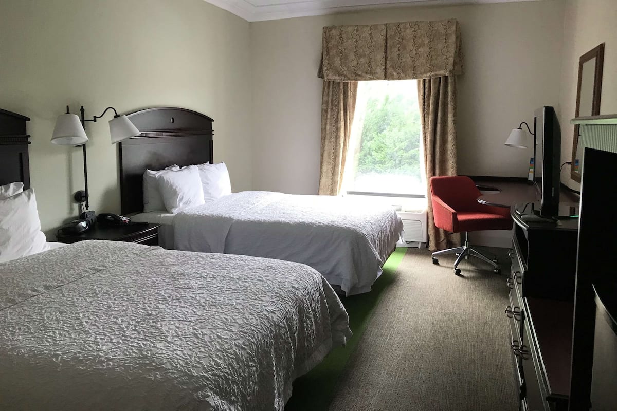 A hotel room with two beds, a desk with a computer, a chair, and a TV.
