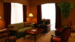 A hotel room with a green sofa, a wooden coffee table, a red armchair, and a patterned carpet. - Hampton Inn Vidalia (Vidalia)