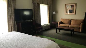 Hotellihuone, jossa on suuri sänky, televisio, sohva, sohvapöytä ja taulu seinällä.