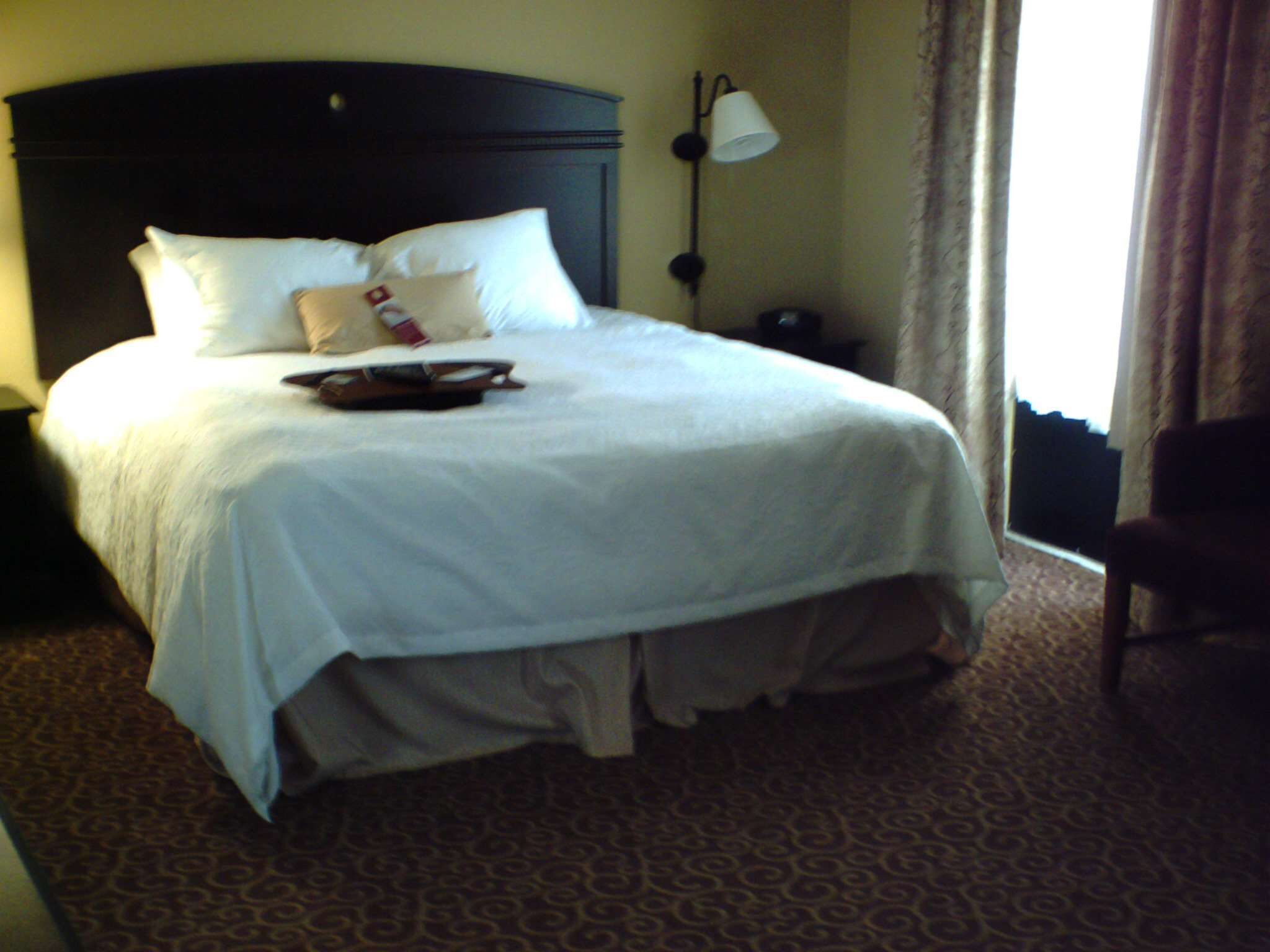 A neatly made bed with white linens, a dark headboard, and a bedside lamp.