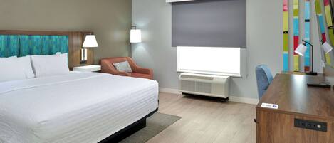Habitación de hotel con una cama grande, un escritorio, una silla, una lámpara, un calentador y una ventana con persianas.