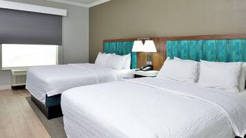 A hotel room with two beds, a nightstand with a lamp, a telephone, and a window with a dark blind.
