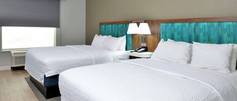 A hotel room with two beds, a nightstand with a lamp, a telephone, and a window with a dark blind.