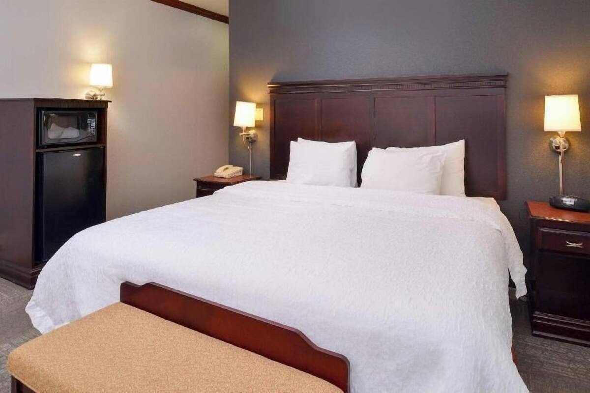 A hotel room with a large bed, bedside lamps, a desk with a telephone, and a microwave.