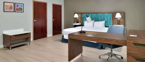 A hotel room with a bed, desk, and two doors.
