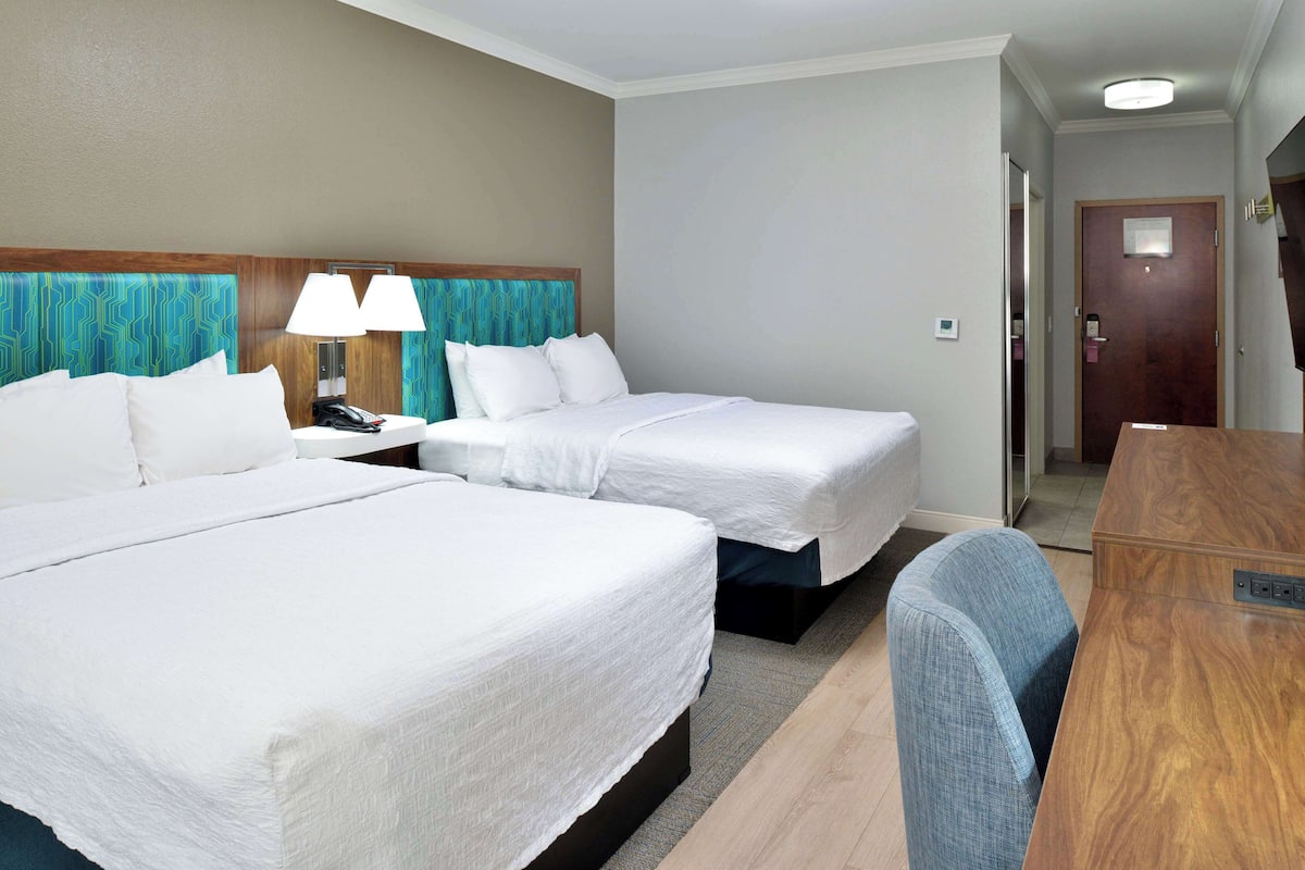 A hotel room with two beds, a desk, and a chair.