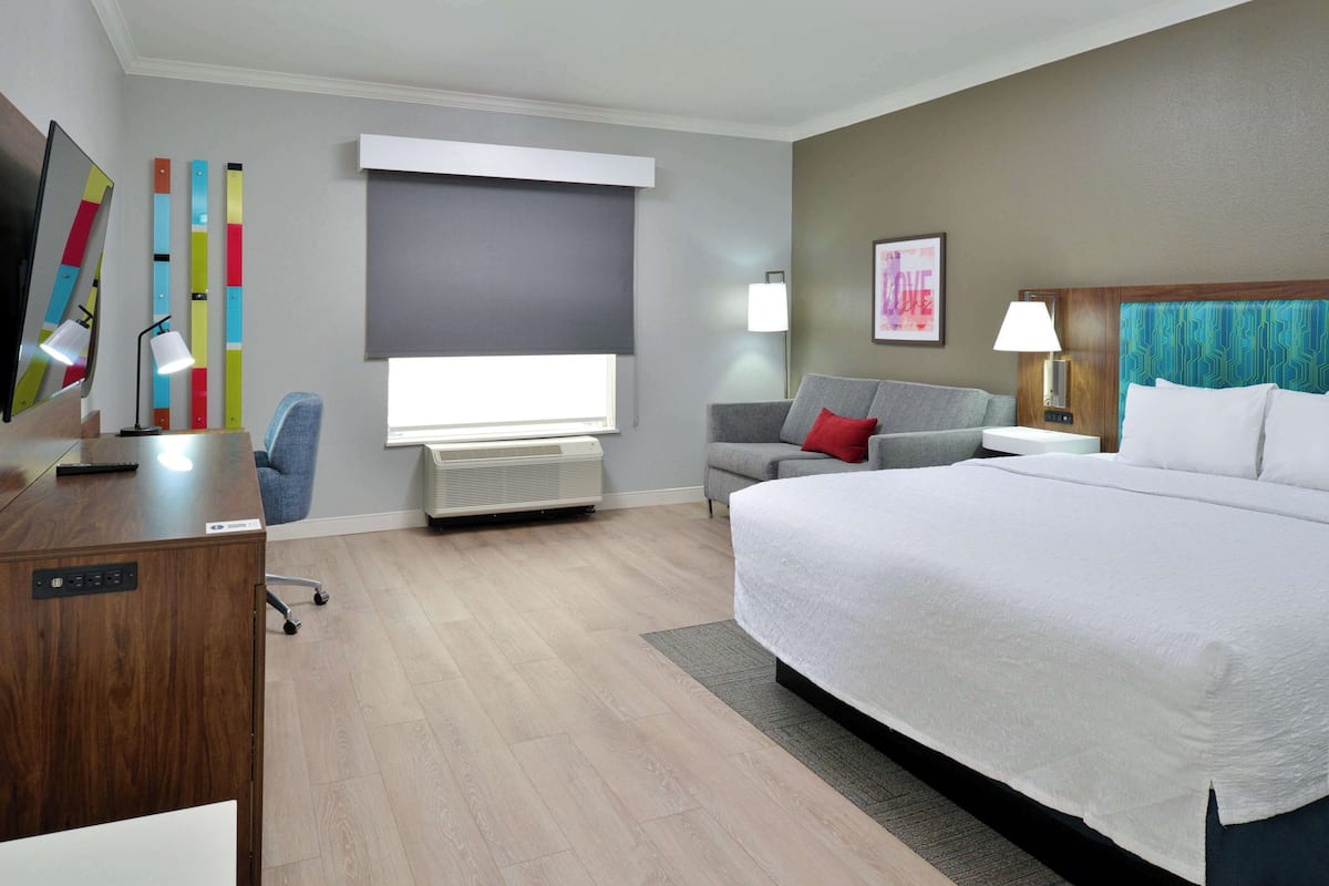 A hotel room with a large bed, a desk with a computer, a chair, a sofa, and a TV.