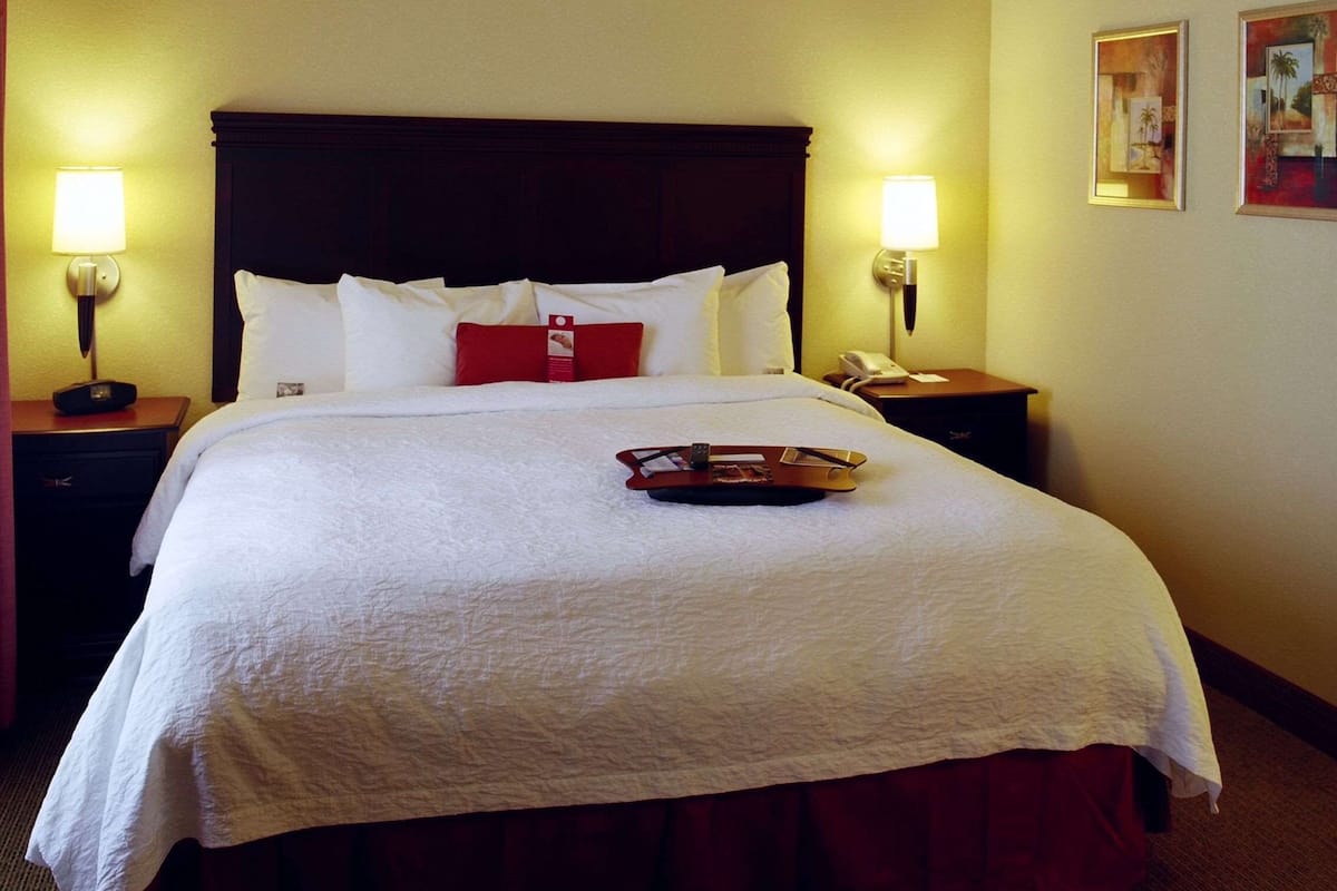 A hotel room with a large bed, two bedside tables, two wall-mounted lamps, and a tray with a remote control on the bed.