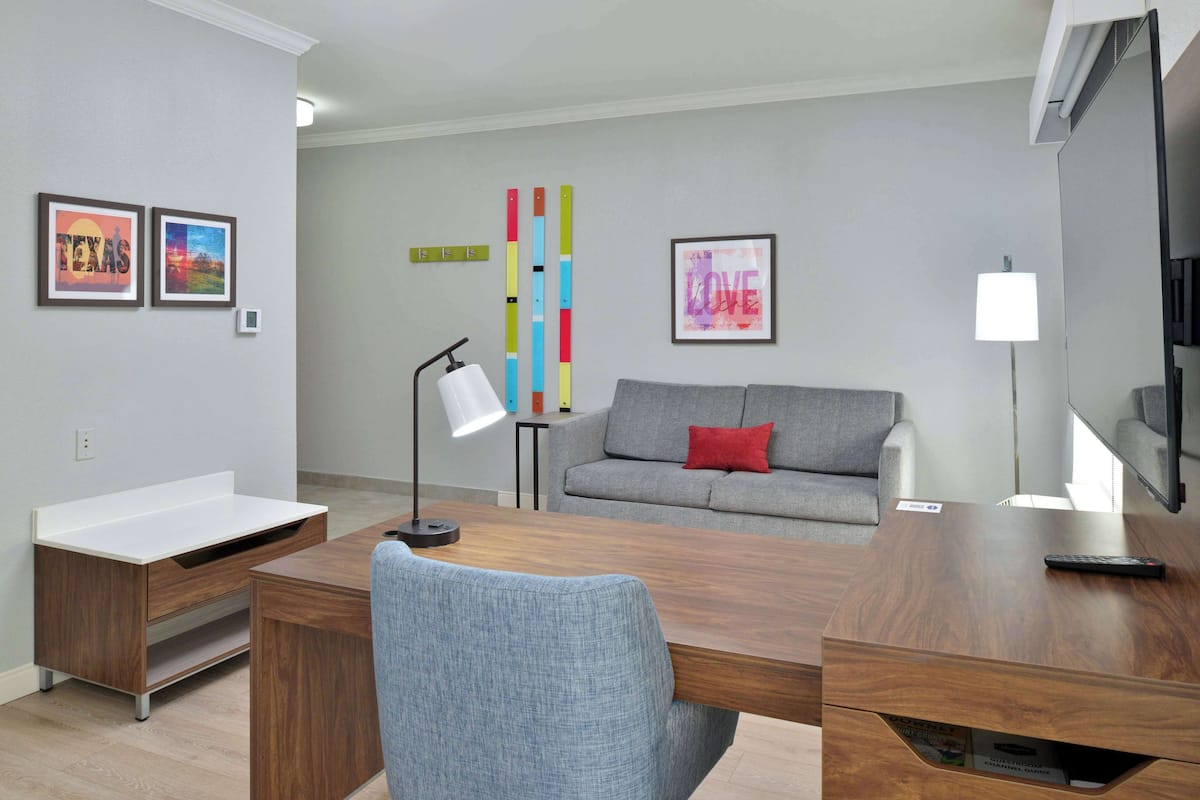 A modern living room with a wooden desk, grey sofa, and colorful artwork on the wall.