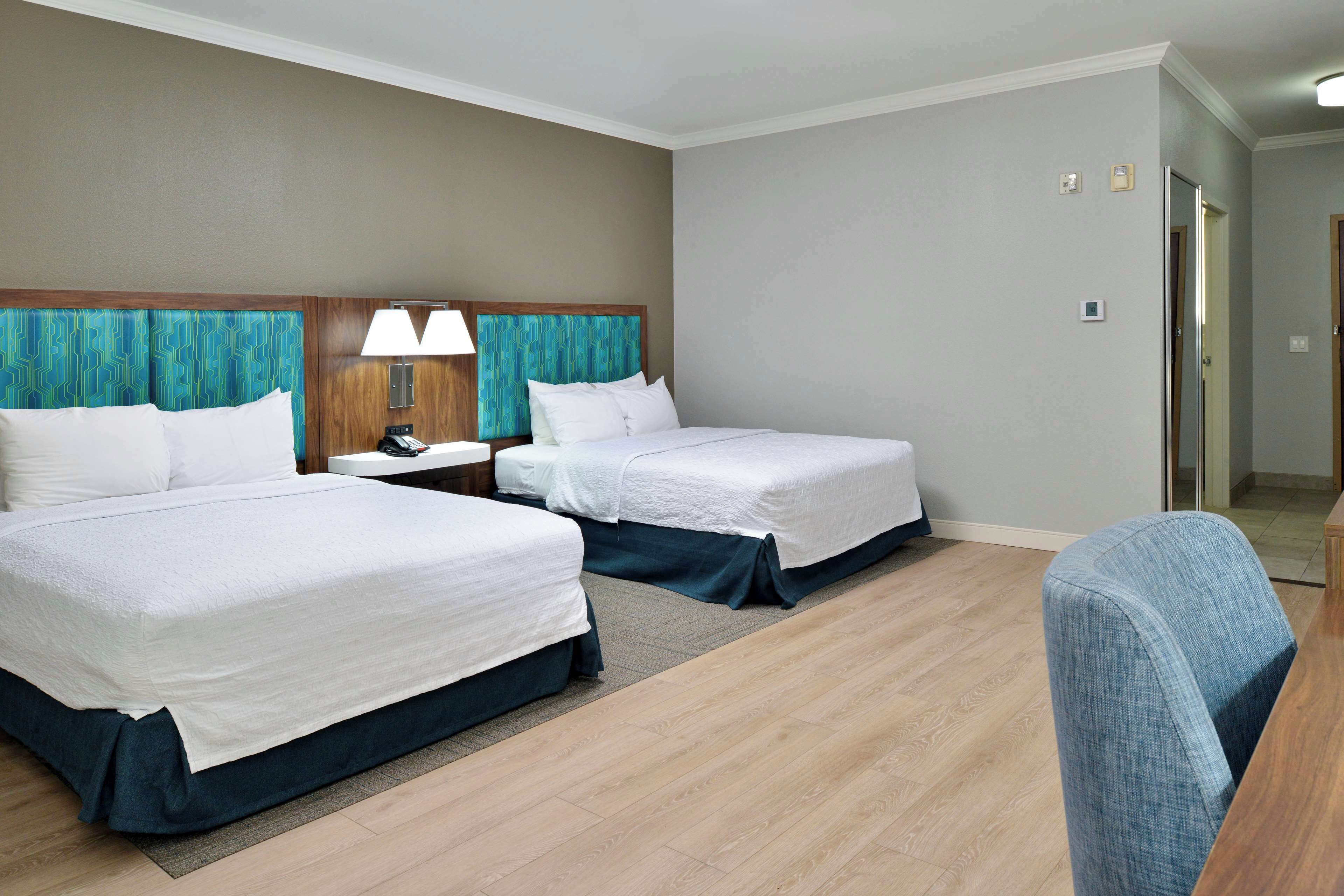 A hotel room with two beds, a nightstand, a desk, and a chair.