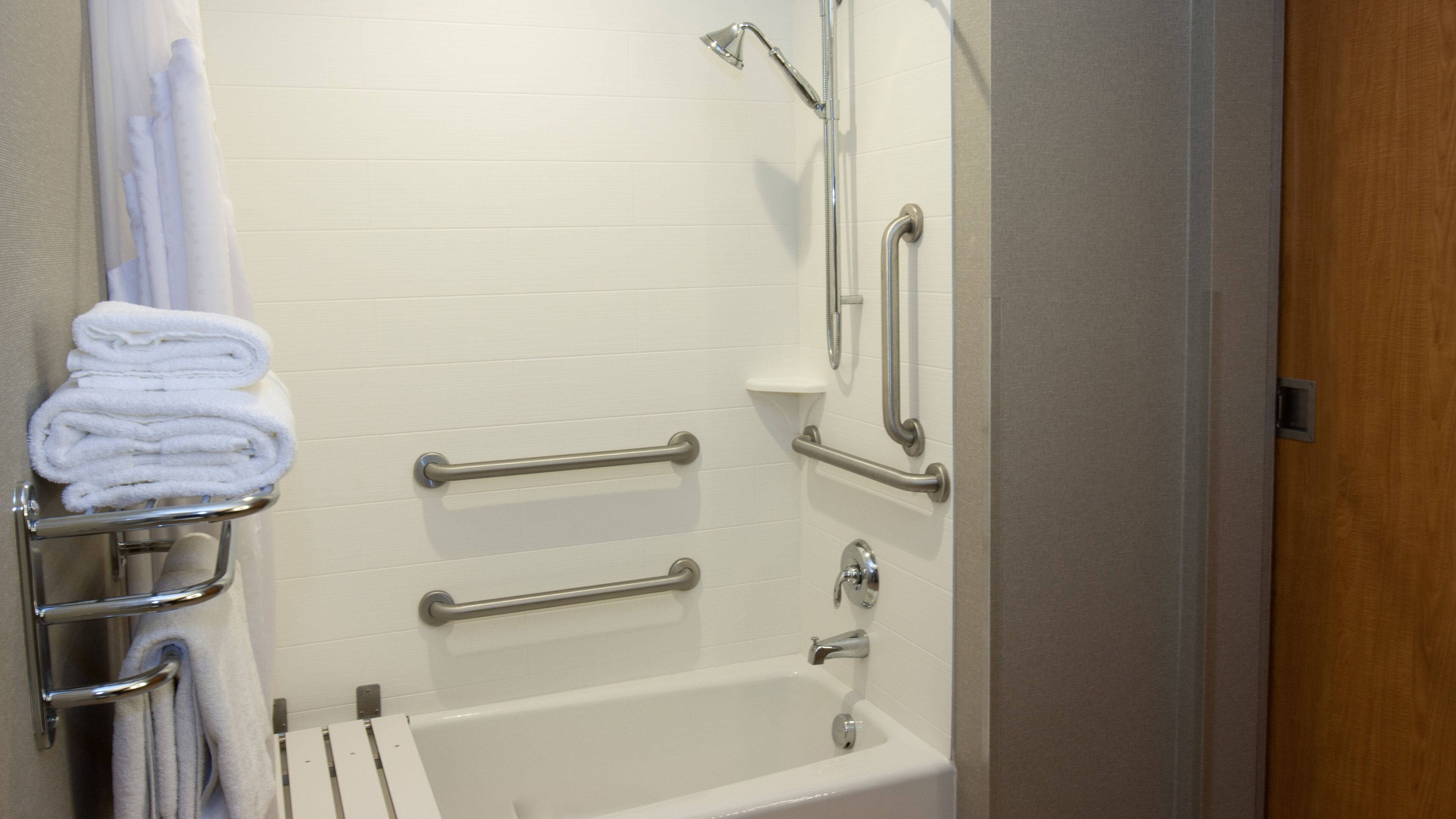 A bathroom with a white bathtub, grab bars, a towel rack, and a shower head.