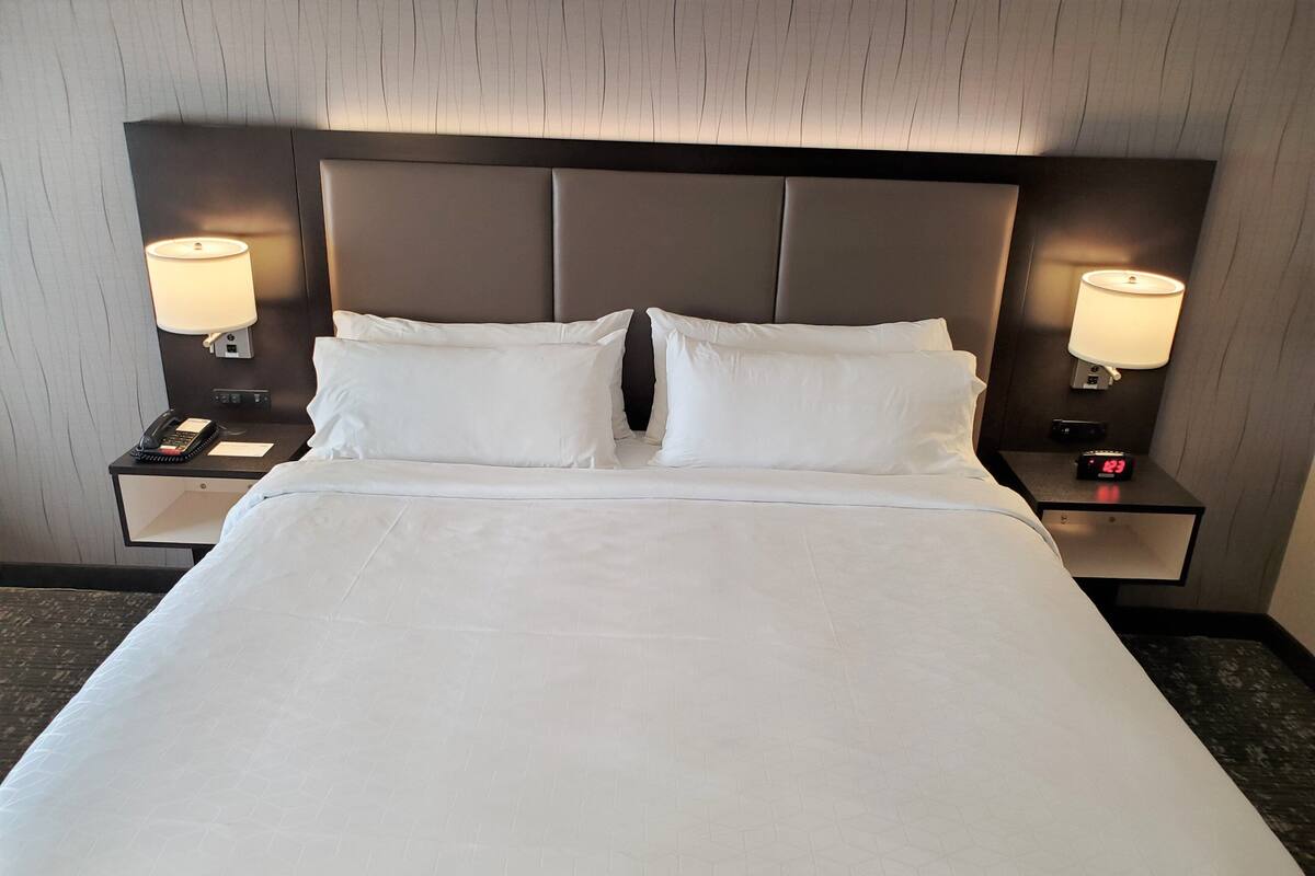 A hotel room with a large bed, two bedside tables, a nightstand, a phone, and a clock.