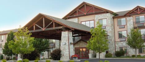 A multi-story hotel with a stone facade, a covered entrance, and a landscaped front yard.
