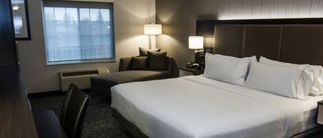 A hotel room with a large bed, a desk, a chair, two bedside lamps, a window, and a wall-mounted heater.