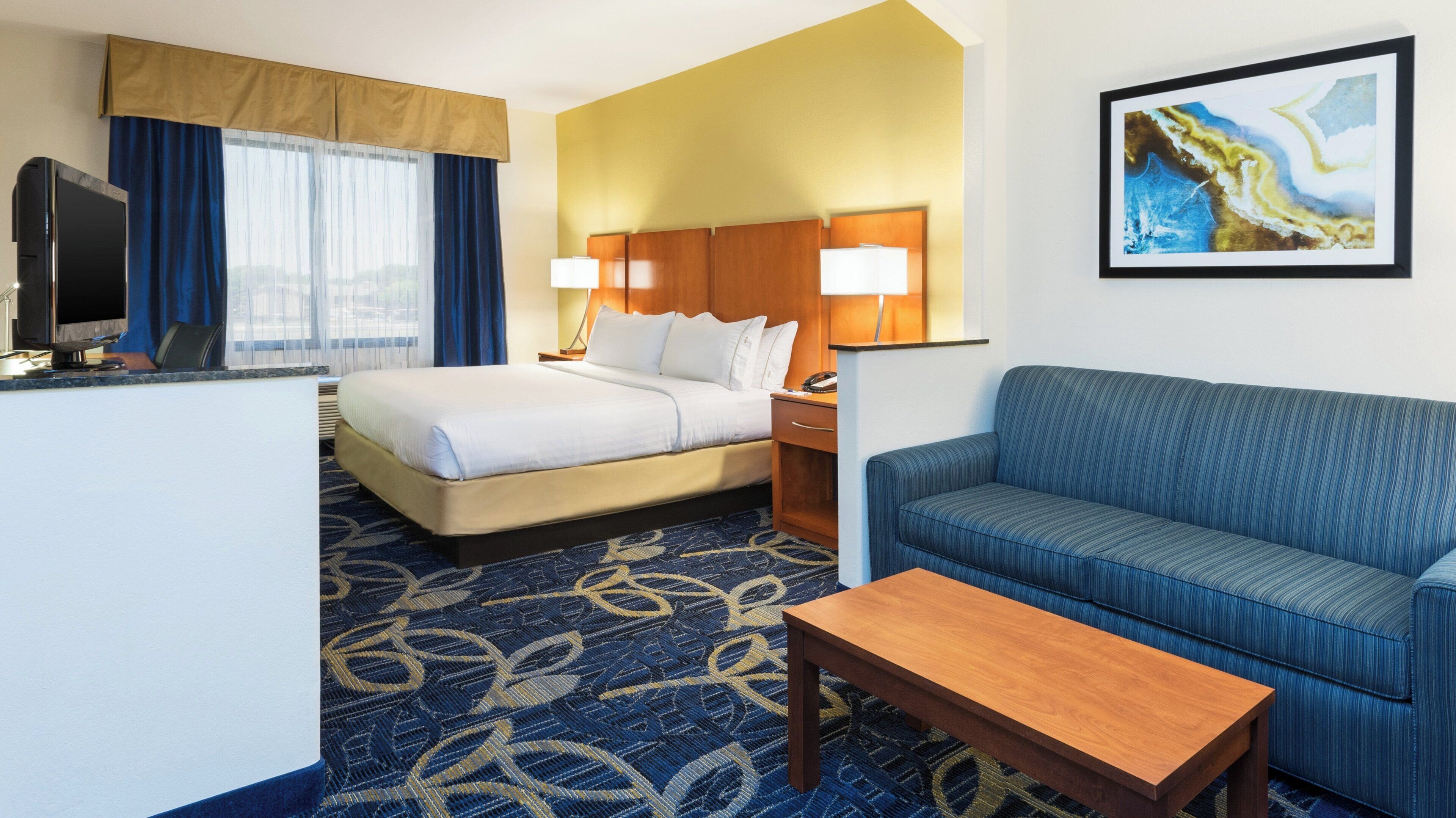 A hotel room with a bed, a sofa, a desk, and a painting on the wall.