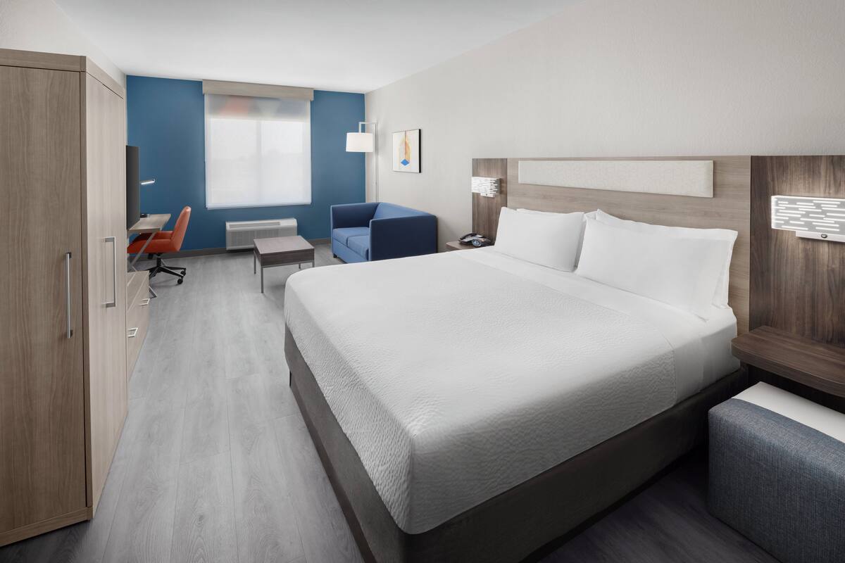 A hotel room with a large bed, a desk, a chair, and a wardrobe.