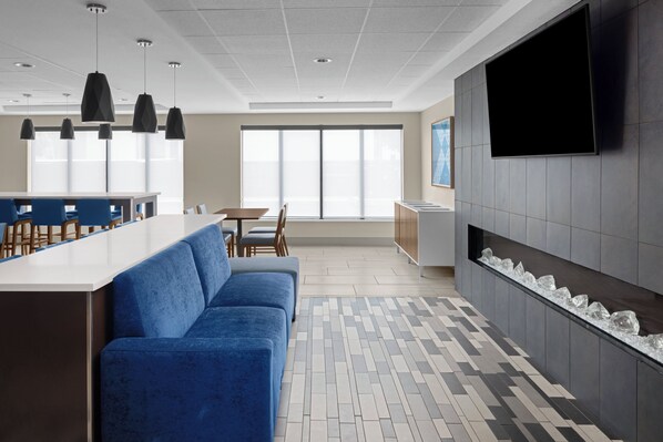 A modern kitchen with a blue sofa, a dining area, and a large TV mounted on the wall. - Holiday Inn Express & Suites Midland Loop 250 by IHG (Midland)