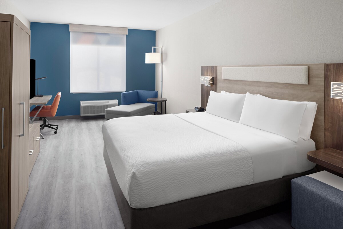 A hotel room with a large bed, a desk with a chair, a small table, and a sofa.