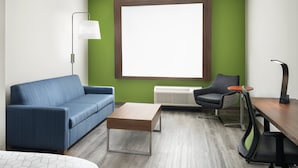 Quarto moderno com sofá azul, mesa de centro de madeira, escrivaninha com cadeira e janela grande com moldura marrom.