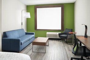 A modern room with a blue sofa, a wooden coffee table, a desk with a chair, and a large window with a brown frame.