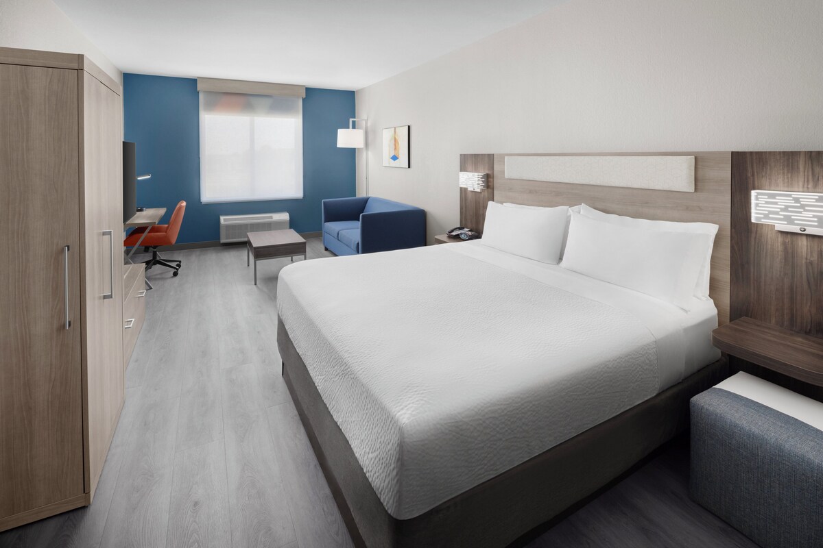 A hotel room with a large bed, a desk, a chair, and a wardrobe.