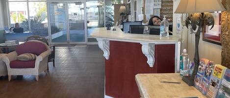 A reception area with a counter, a desk, and a chair. There is a lamp on the desk and a framed picture on the wall.