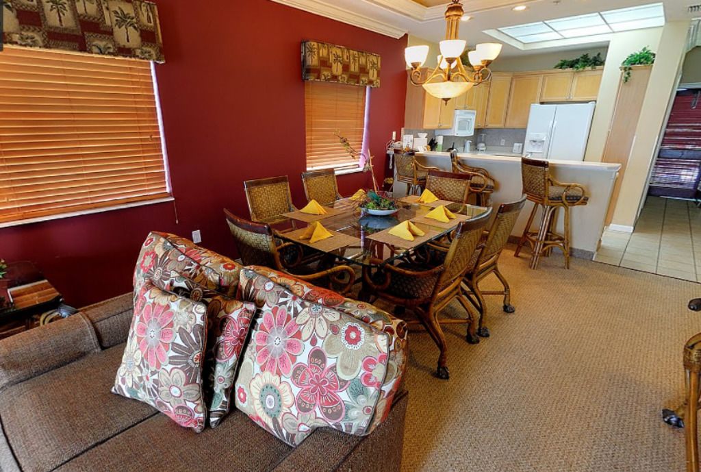 A dining area with a table set for four, surrounded by wicker chairs and a sofa with floral cushions.