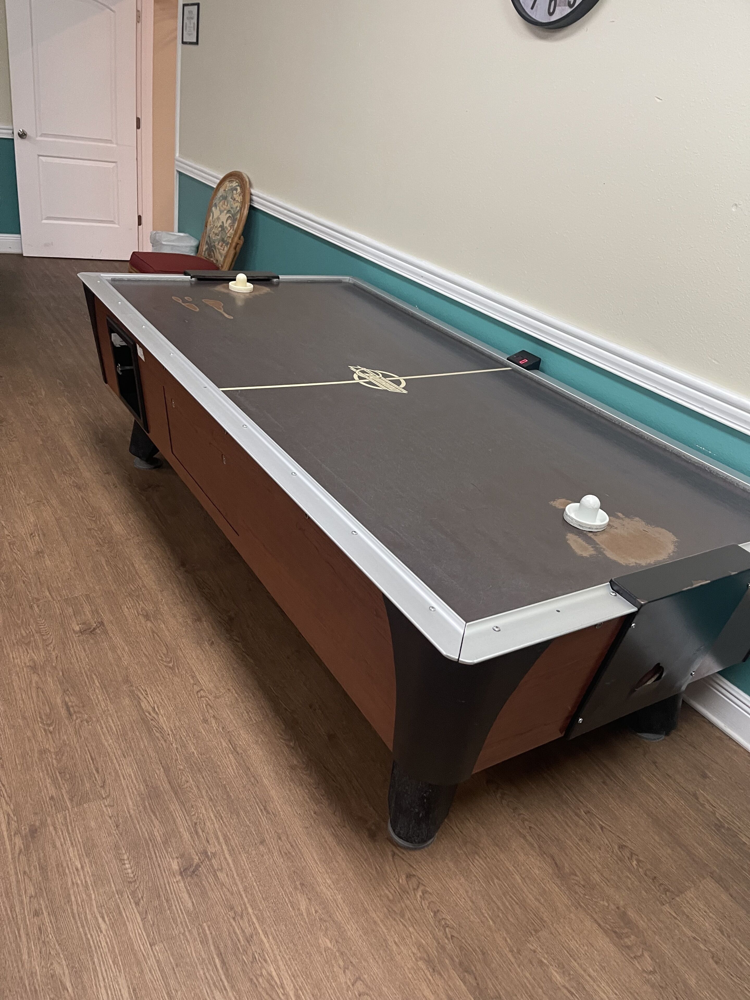 A pool table with a white border, a logo in the center, and a clock on the wall.