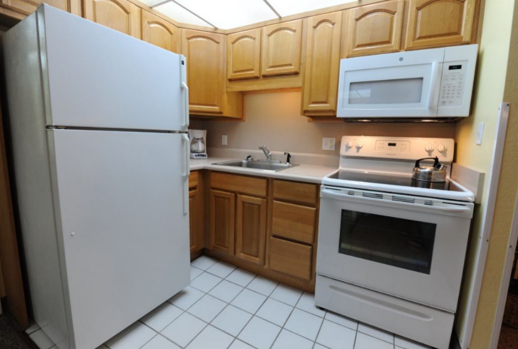Une cuisine avec des meubles de rangement en bois, un réfrigérateur blanc, un four à micro-ondes, un évier et une cuisinière.
