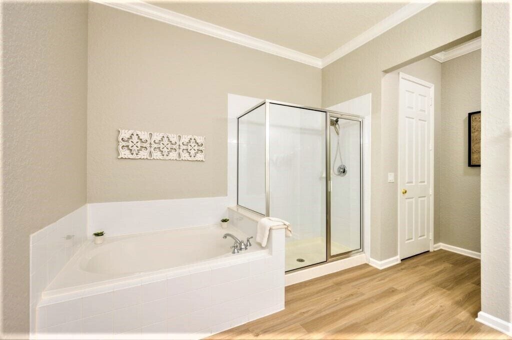 Un baño con una bañera grande, una cabina de ducha de vidrio y una puerta blanca.