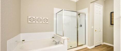 Un baño con una bañera grande, una cabina de ducha de vidrio y una puerta blanca.