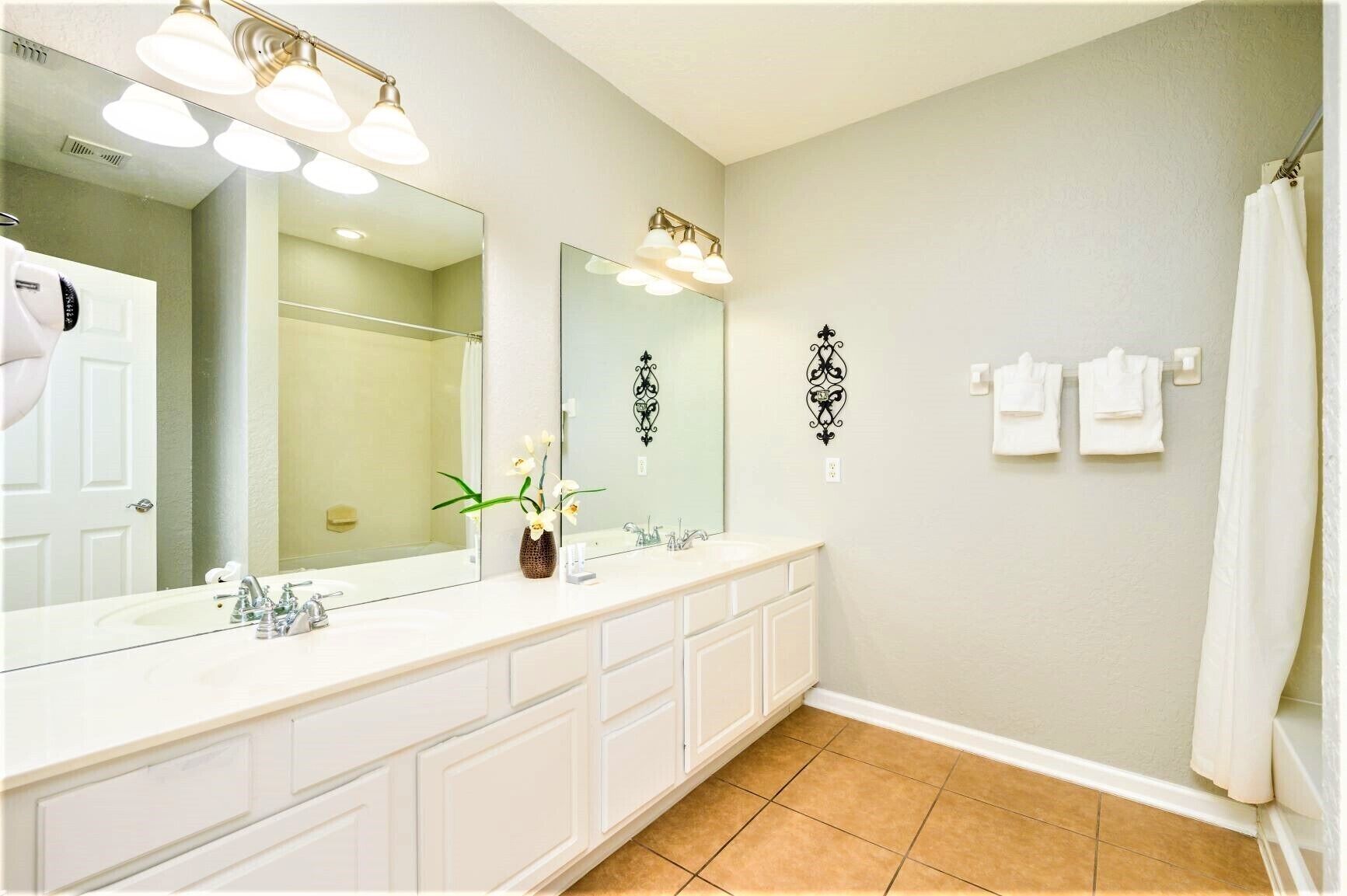 A bathroom with a large mirror, two sinks, a shower, and a towel rack.