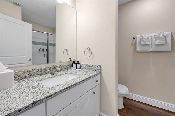 A bathroom with a granite countertop, a sink, a toilet, and a towel rack with towels.