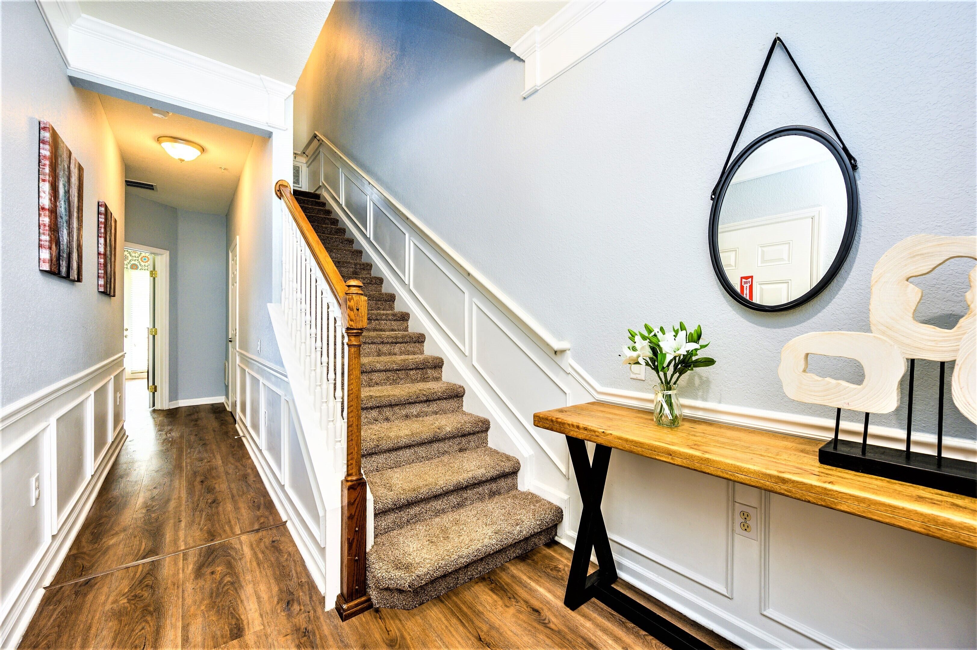 A staircase with wooden steps and white railings, leading to a landing with a wooden table and a vase of flowers.