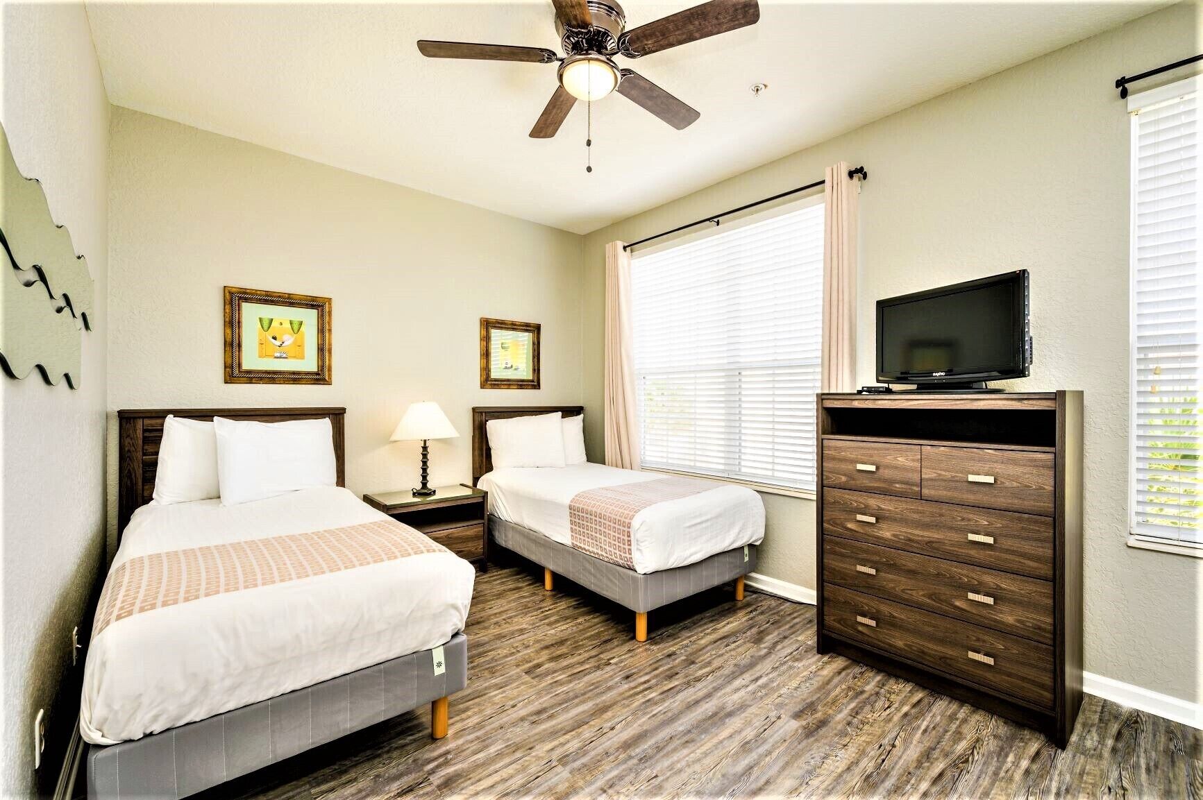 A hotel room with two beds, a ceiling fan, a TV, and a dresser.