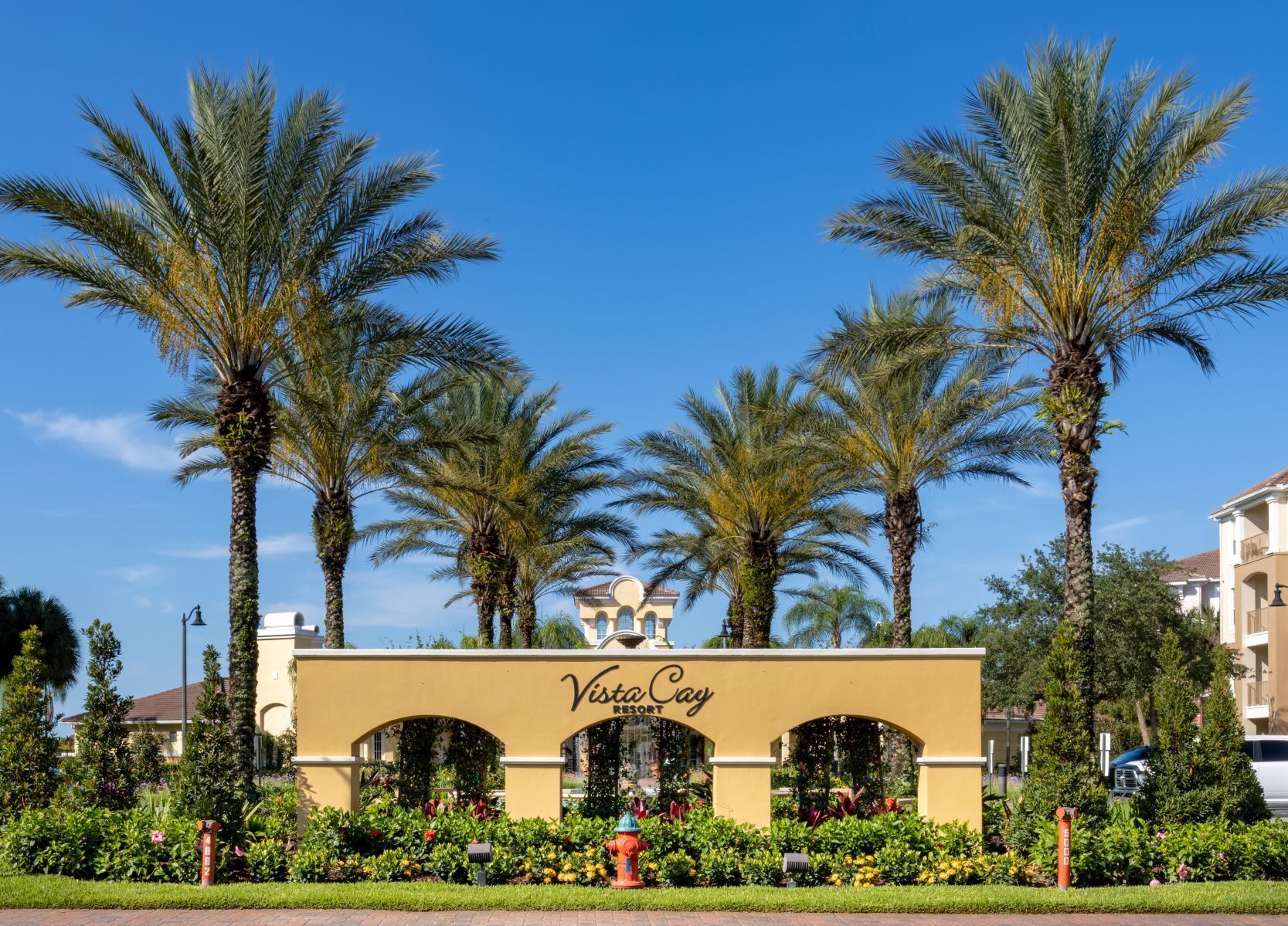 L’entrée d’un complexe hôtelier, avec des palmiers, une arche jaune et l’inscription « Vista Cay Resort ».