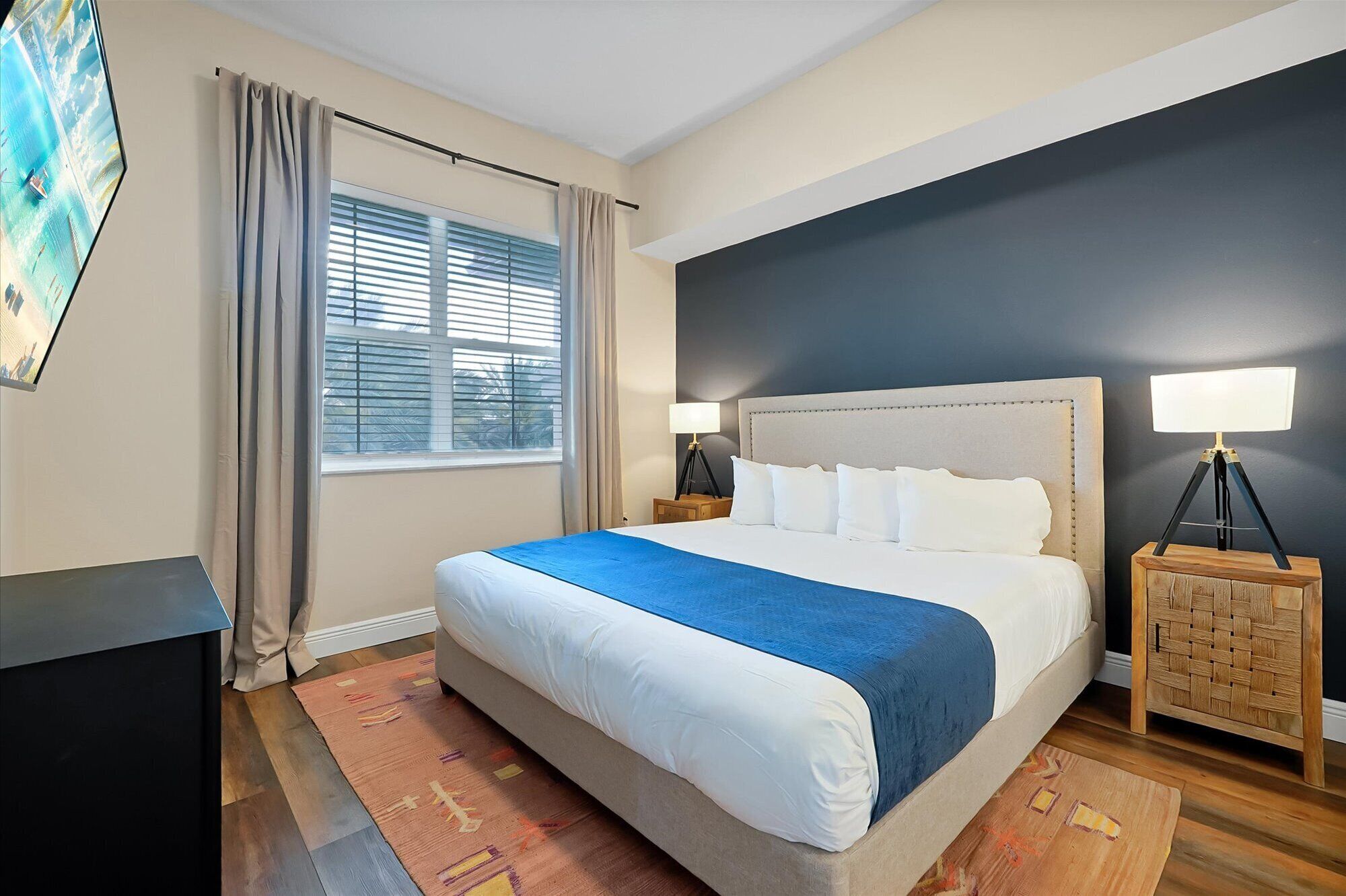 A hotel room with a bed, a desk, a lamp, and a window with curtains.