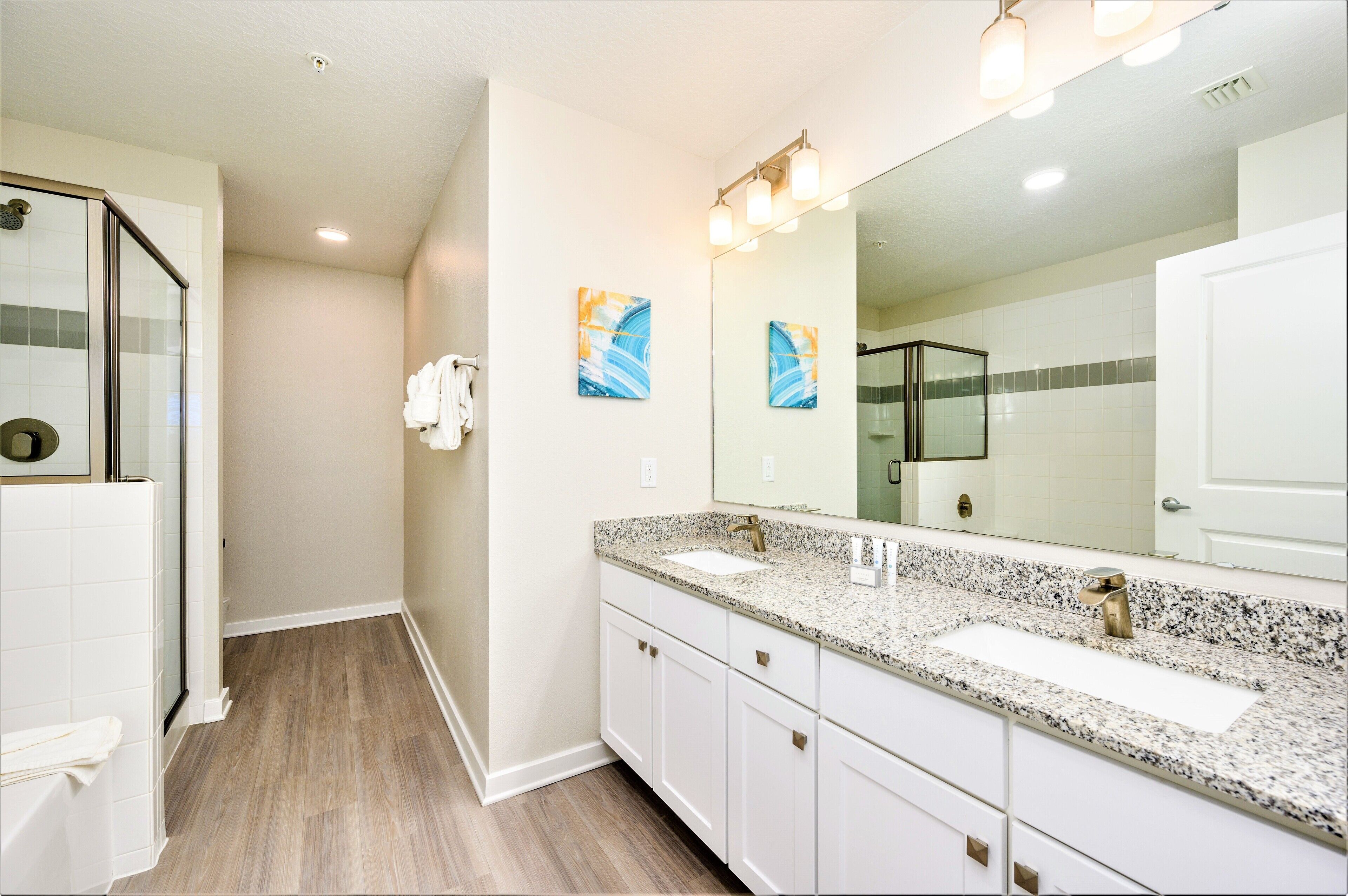 A modern bathroom with a large mirror, two sinks, and a shower area.