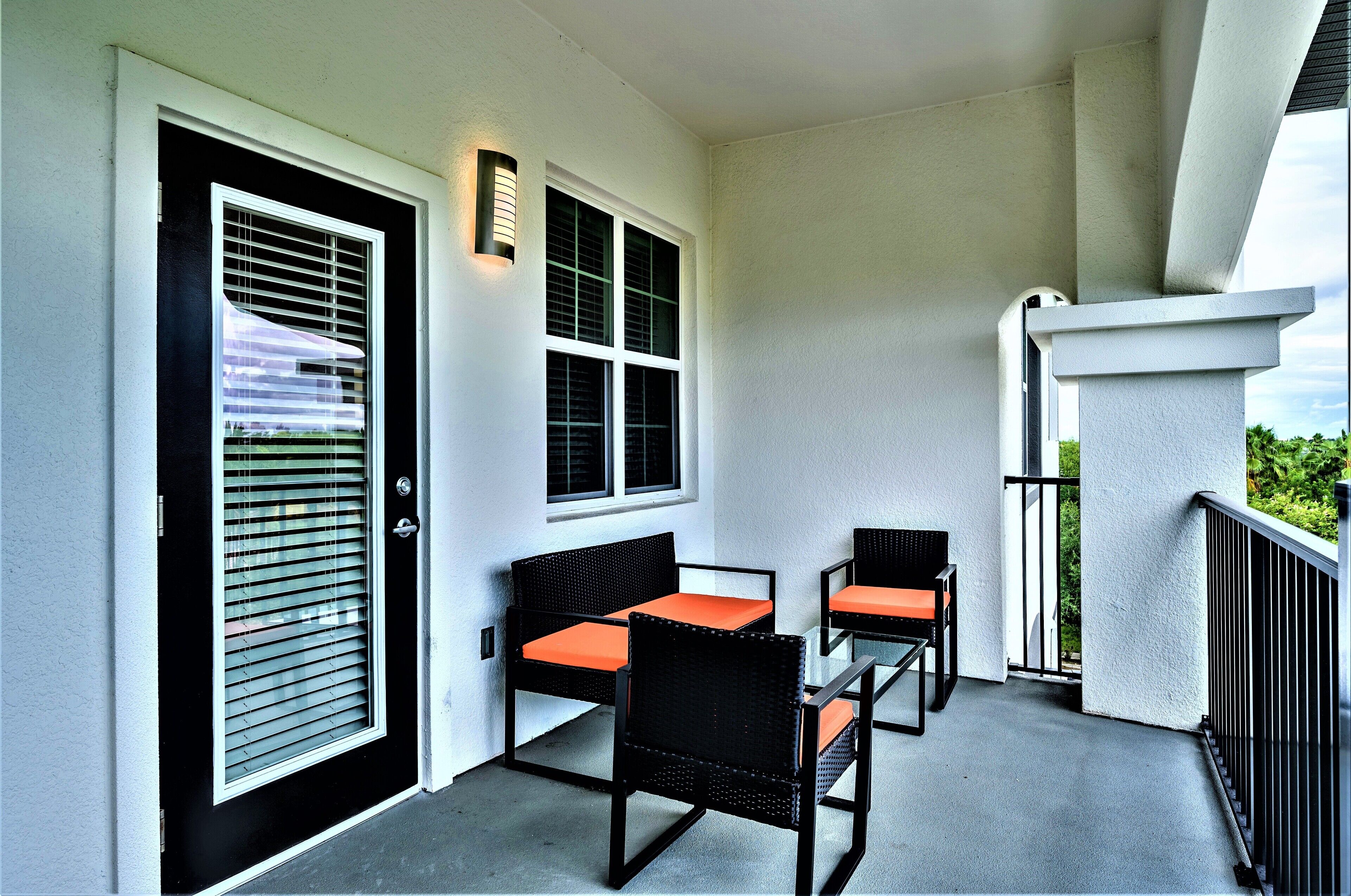 A balcony with two chairs and a table, a door with a window, and a wall-mounted light fixture.