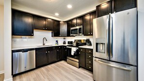 Une cuisine moderne avec des meubles de couleur sombre en bois, des appareils électroménagers en acier inoxydable et un plancher en bois clair.