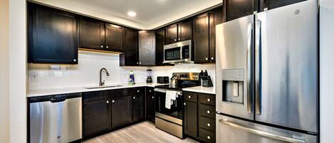 A modern kitchen with dark wooden cabinets, stainless steel appliances, and a light wood floor.