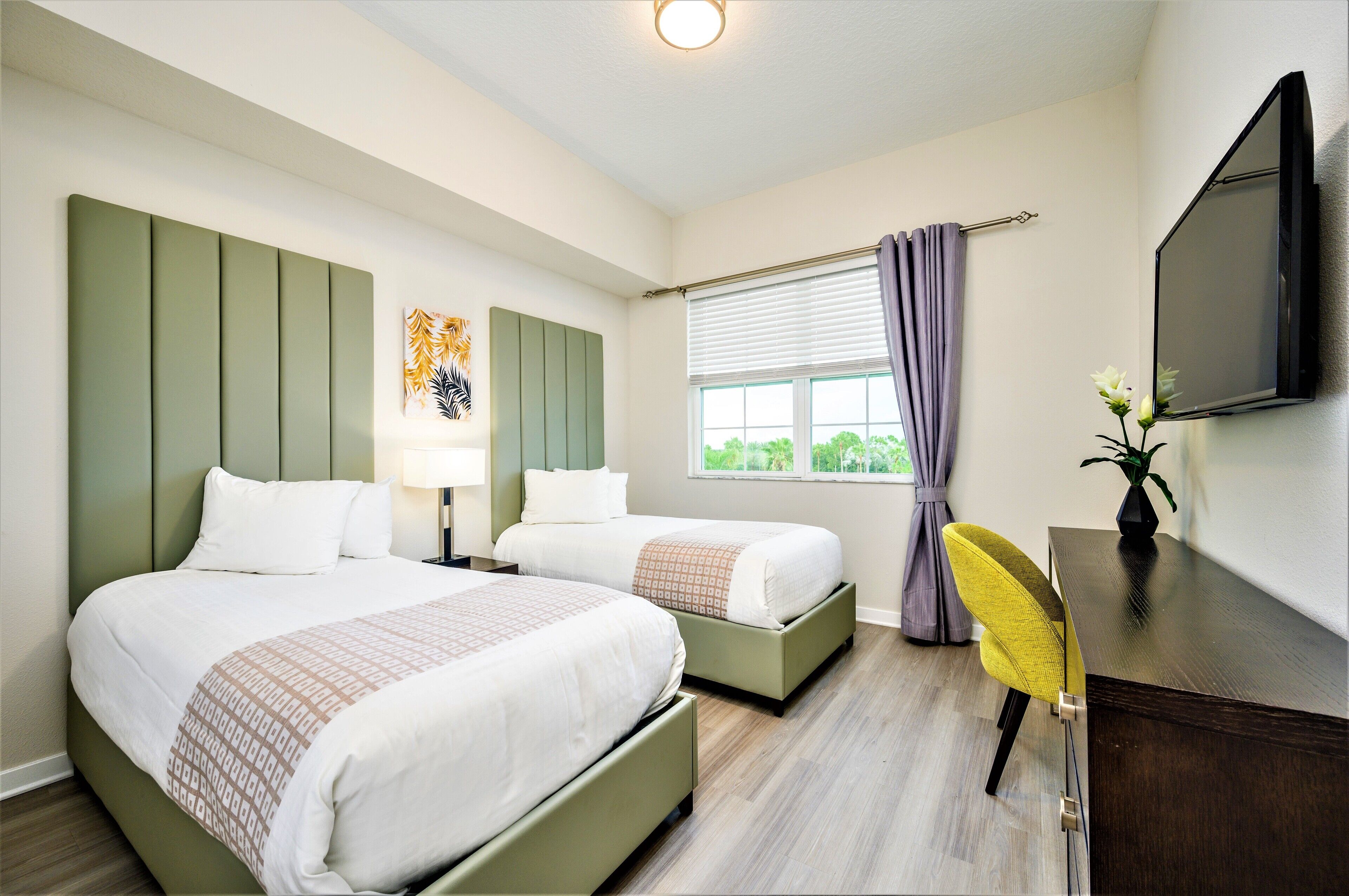 A hotel room with two beds, a desk, a chair, a TV, and a window with curtains.