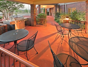 Un patio al aire libre con una parrilla, mesas y sillas.