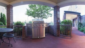 An outdoor patio with a stainless steel grill, a round table with chairs, and a brick pillar. - Candlewood Suites West Little Rock by IHG (Little Rock)