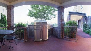 An outdoor patio with a stainless steel grill, a round table with chairs, and a brick pillar. - Candlewood Suites West Little Rock by IHG (Little Rock)