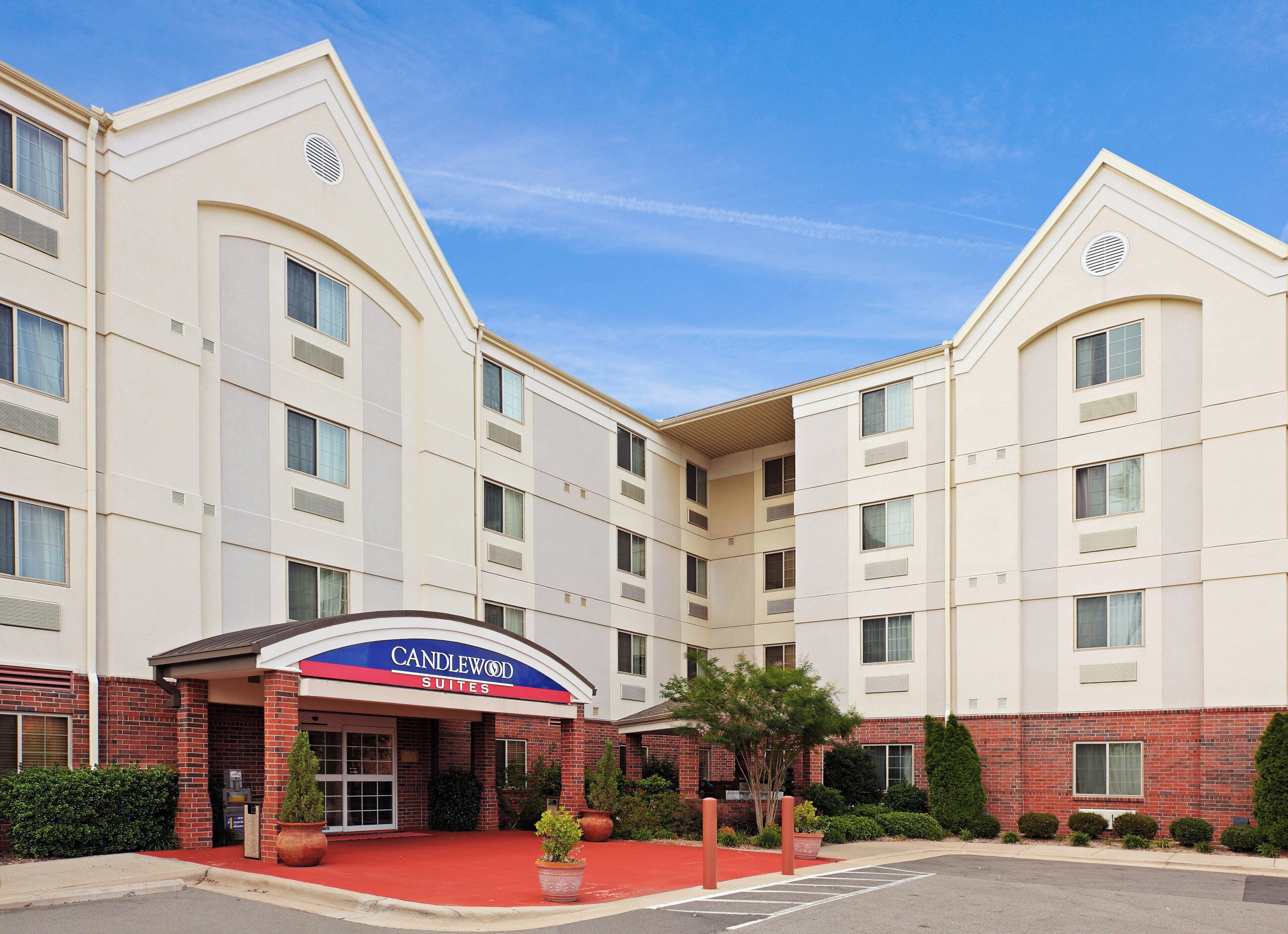 Un hotel con un cartello ben visibile 'Candlewood Suites', diversi piani e un'area d'ingresso rossa.