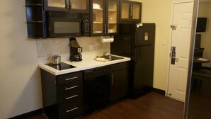 A compact kitchen with dark cabinetry, a microwave, a refrigerator, and a dishwasher. - Candlewood Suites West Little Rock by IHG (Little Rock)