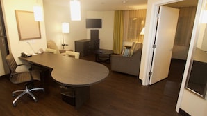 A hotel room with a large round table, a sofa, a TV, and a door leading to another room. - Candlewood Suites West Little Rock by IHG (Little Rock)