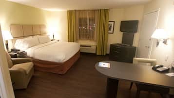 Habitación de hotel con cama, escritorio, silla, televisión y ventana con cortinas.